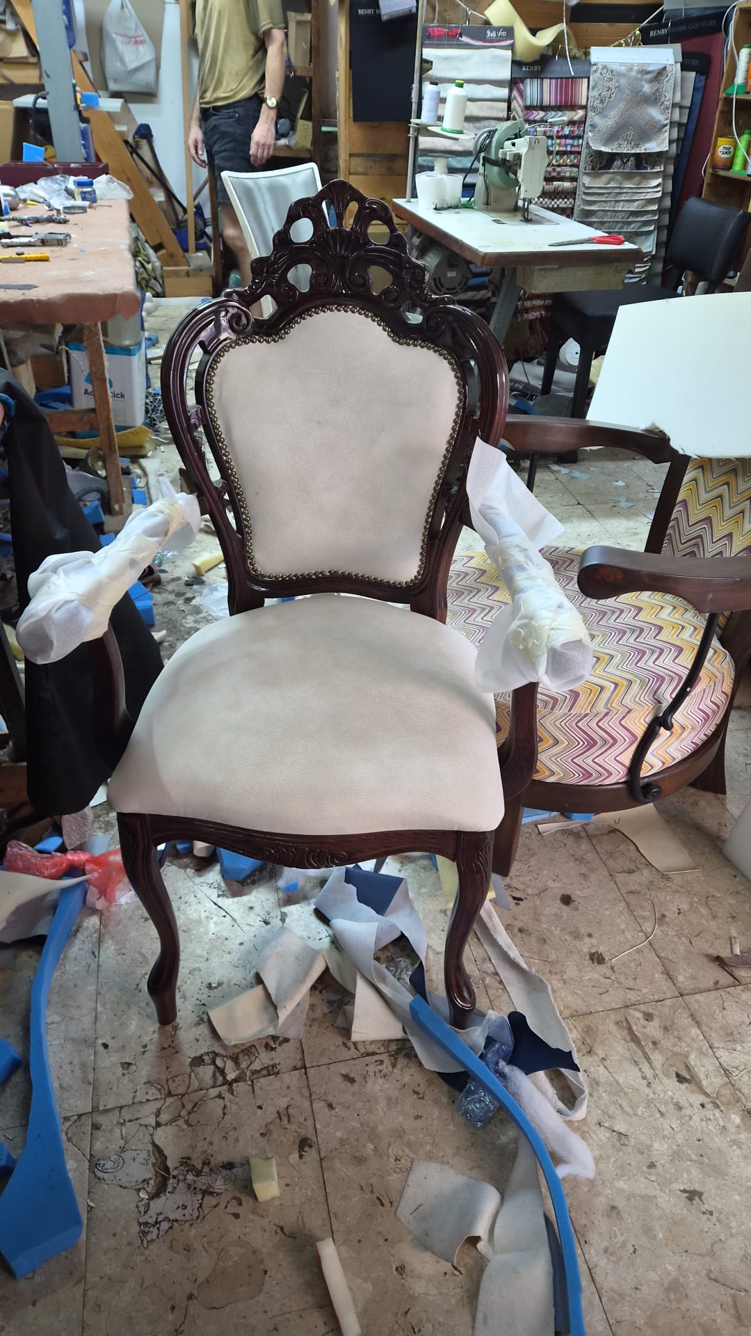 כורסת עץ מגולפת עתיקה לאחר ריפוד בבד בז' עם נעצי פליז, בבית המלאכה